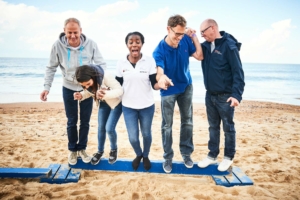 participants sur une poutre réalisant main dans la main une épreuve du Beach & Water Olympics