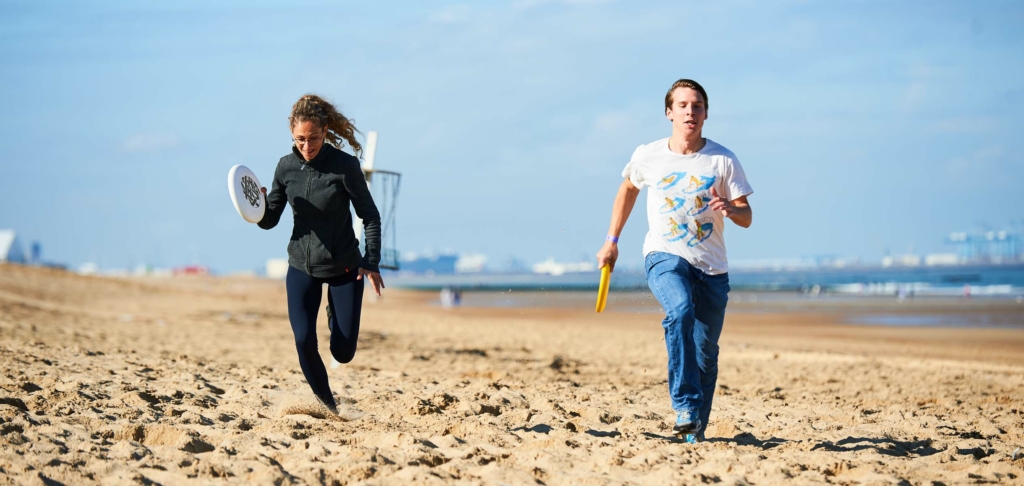 participants courant sur la plage avec une frisbee en main lors du Beach & Water Olympics