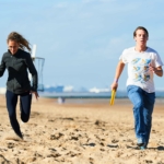 participants running on the beach with a frisbee in hand during the Beach Olympics