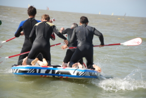 participants pagayant ensemble sur un surf géant du Water Games